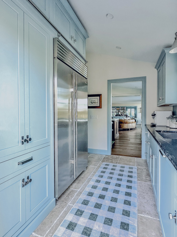 Cette image montre une cuisine parallèle traditionnelle de taille moyenne avec un évier posé, un placard à porte shaker, des portes de placard bleues, un plan de travail en granite, un électroménager en acier inoxydable, un sol beige et plan de travail noir.