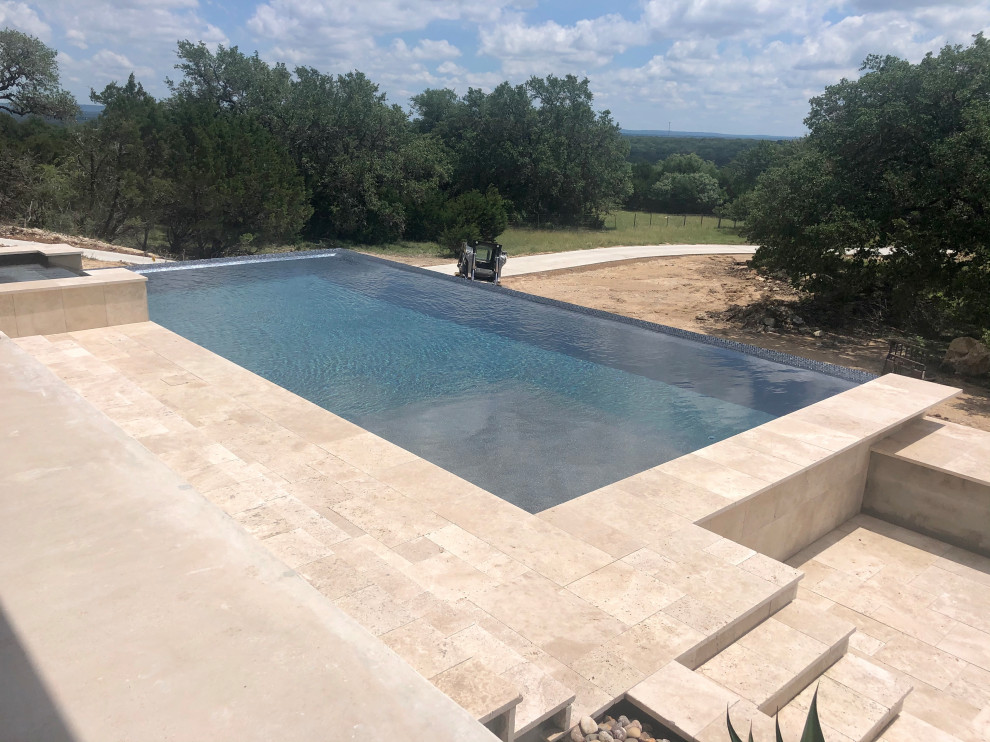 Inspiration for an expansive modern backyard rectangular infinity pool in Austin with a hot tub and natural stone pavers.