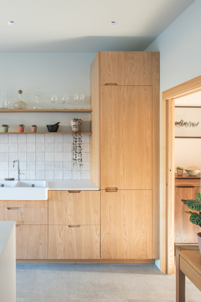 This is an example of a medium sized scandinavian single-wall kitchen/diner in London with a double-bowl sink, flat-panel cabinets, medium wood cabinets, composite countertops, white splashback, ceramic splashback, black appliances, porcelain flooring, an island, grey floors and white worktops.