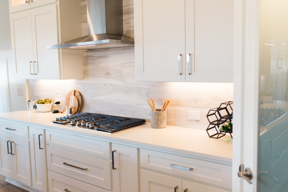 Inspiration for a large transitional l-shaped light wood floor and gray floor open concept kitchen remodel in Phoenix with a drop-in sink, shaker cabinets, white cabinets, quartz countertops, gray backsplash, ceramic backsplash, stainless steel appliances, an island and white countertops