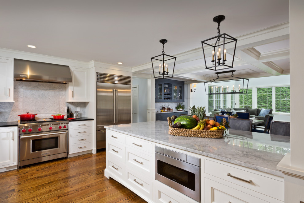 This is an example of an expansive traditional l-shaped eat-in kitchen in Boston with a farmhouse sink, beaded inset cabinets, white cabinets, marble benchtops, grey splashback, marble splashback, stainless steel appliances, medium hardwood floors, with island, brown floor, grey benchtop and coffered.
