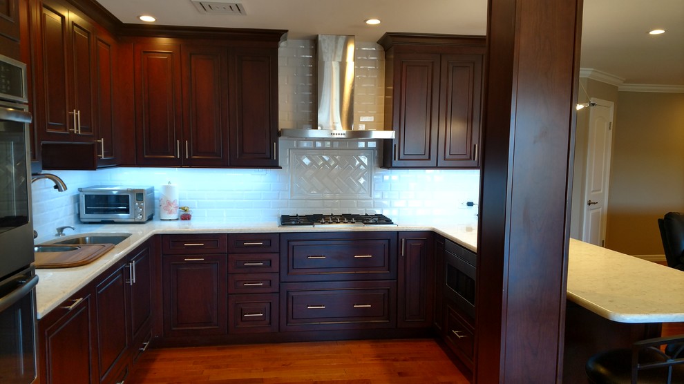 Example of a large transitional u-shaped medium tone wood floor kitchen design in New York with raised-panel cabinets, dark wood cabinets, white backsplash, subway tile backsplash, stainless steel appliances, a peninsula and an undermount sink