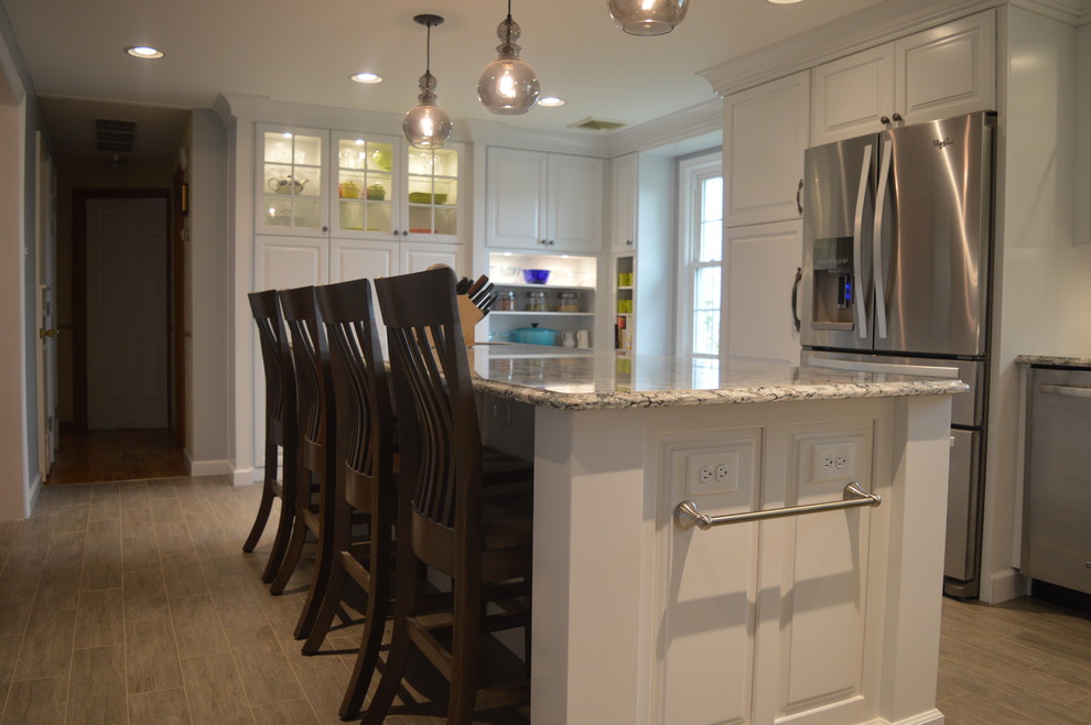 Large transitional u-shaped ceramic tile and gray floor home design photo with a farmhouse sink, raised-panel cabinets, white cabinets, quartz countertops, gray backsplash, glass tile backsplash, stainless steel appliances and an island