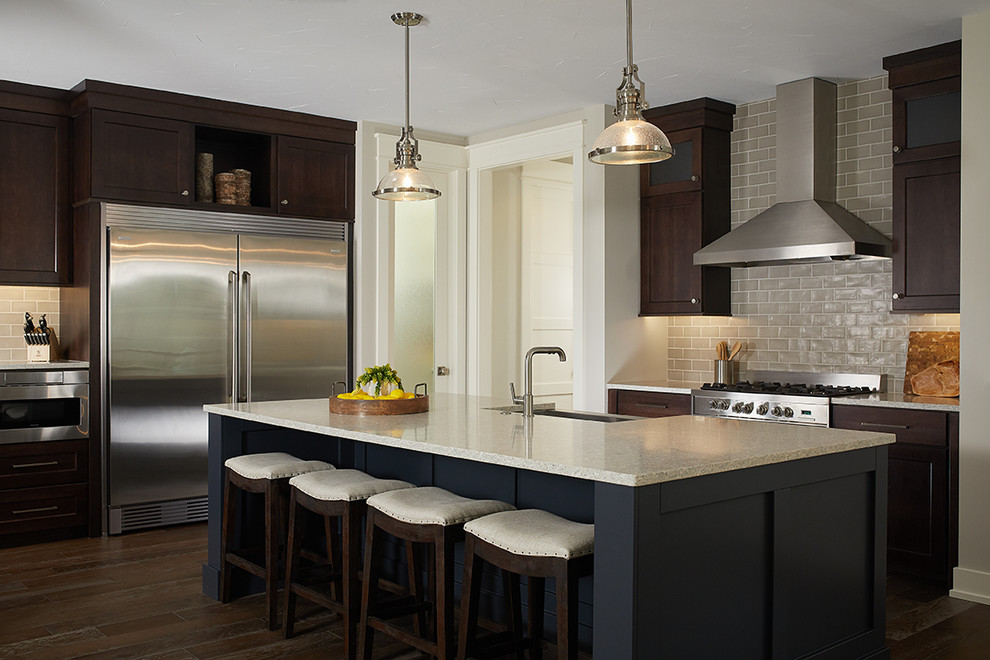 This is an example of a transitional separate kitchen in Grand Rapids with shaker cabinets, dark wood cabinets, grey splashback, subway tile splashback, stainless steel appliances, dark hardwood floors, with island and brown floor.