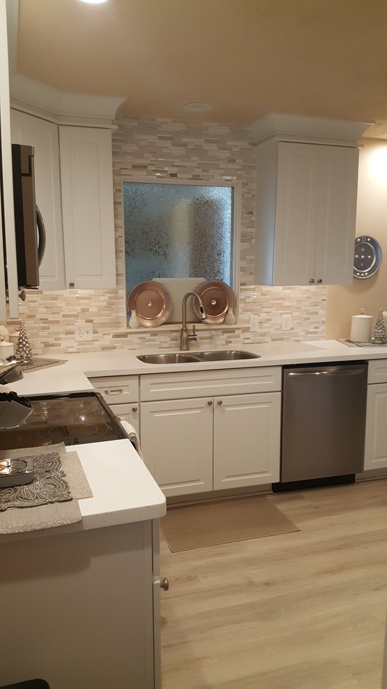 Example of a small l-shaped eat-in kitchen design with an undermount sink, raised-panel cabinets, white cabinets, quartz countertops, white backsplash, porcelain backsplash, stainless steel appliances and no island