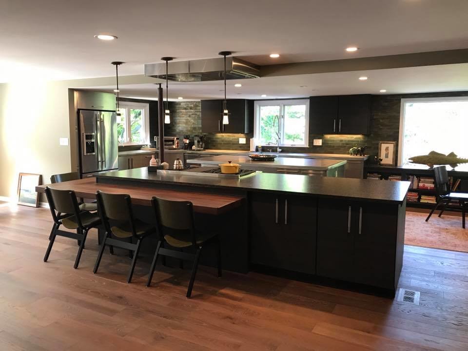 This is an example of a large modern l-shaped eat-in kitchen in New York with an undermount sink, flat-panel cabinets, black cabinets, green splashback, subway tile splashback, stainless steel appliances, dark hardwood floors, multiple islands, brown floor and zinc benchtops.