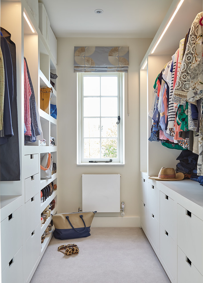 This is an example of a mid-sized contemporary gender-neutral walk-in wardrobe in London with flat-panel cabinets, white cabinets, carpet and beige floor.