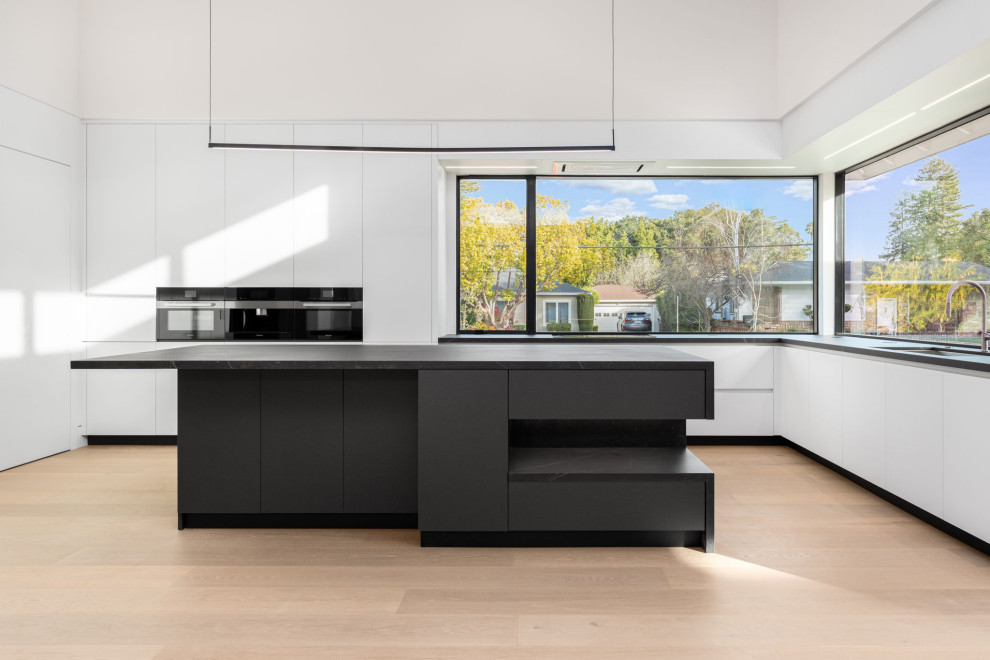 Large modern galley open plan kitchen in San Francisco with a submerged sink, flat-panel cabinets, white cabinets, engineered stone countertops, black appliances, an island and black worktops.