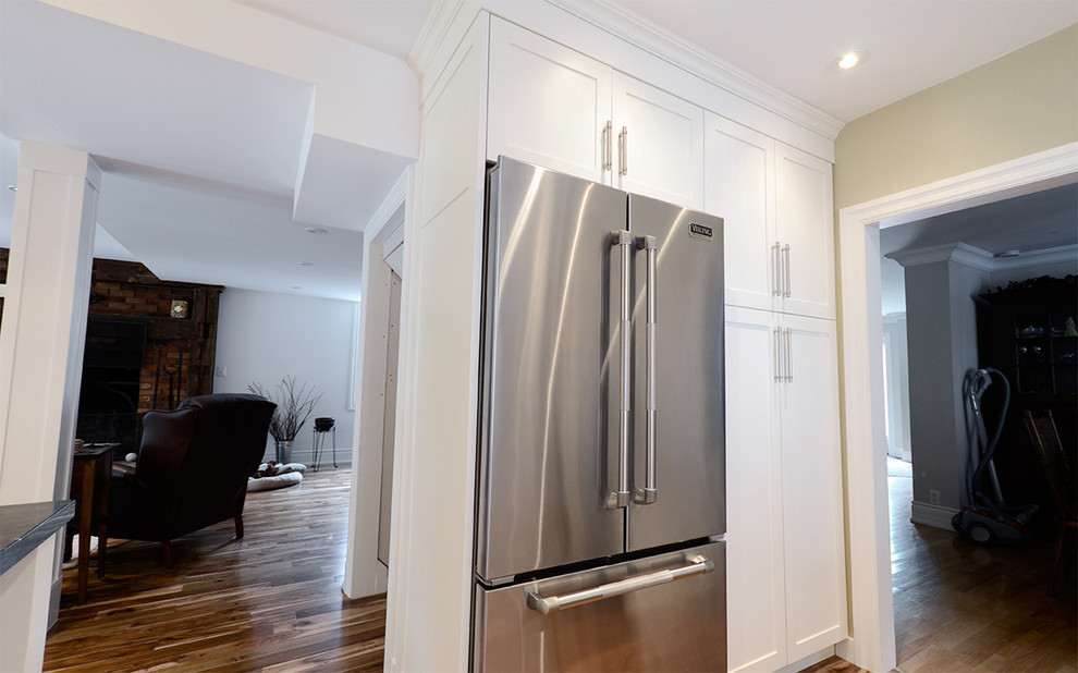 Inspiration for a mid-sized transitional l-shaped medium tone wood floor eat-in kitchen remodel in Toronto with a double-bowl sink, raised-panel cabinets, white cabinets, solid surface countertops, black backsplash, stone slab backsplash, stainless steel appliances and an island