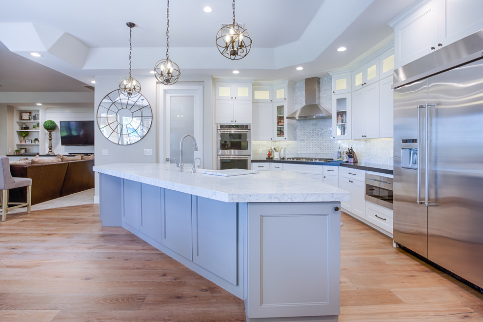 Mid-sized country single-wall eat-in kitchen in Phoenix with a farmhouse sink, shaker cabinets, white cabinets, white splashback, marble splashback, stainless steel appliances, medium hardwood floors, with island, brown floor and white benchtop.