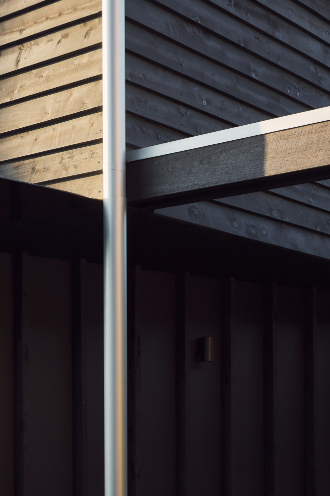 Idée de décoration pour une façade de maison noire minimaliste en bois et bardage à clin de taille moyenne et à un étage avec un toit à deux pans et un toit en métal.