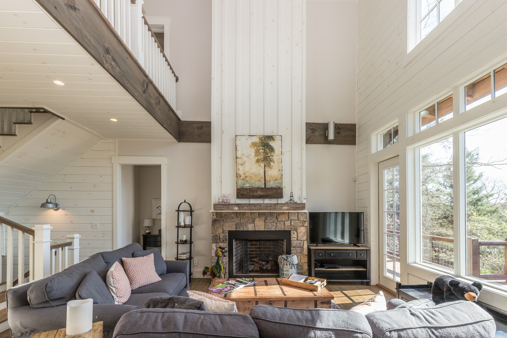 Inspiration for a country living room in Other with white walls, medium hardwood floors, a standard fireplace, a stone fireplace surround, a freestanding tv and brown floor.