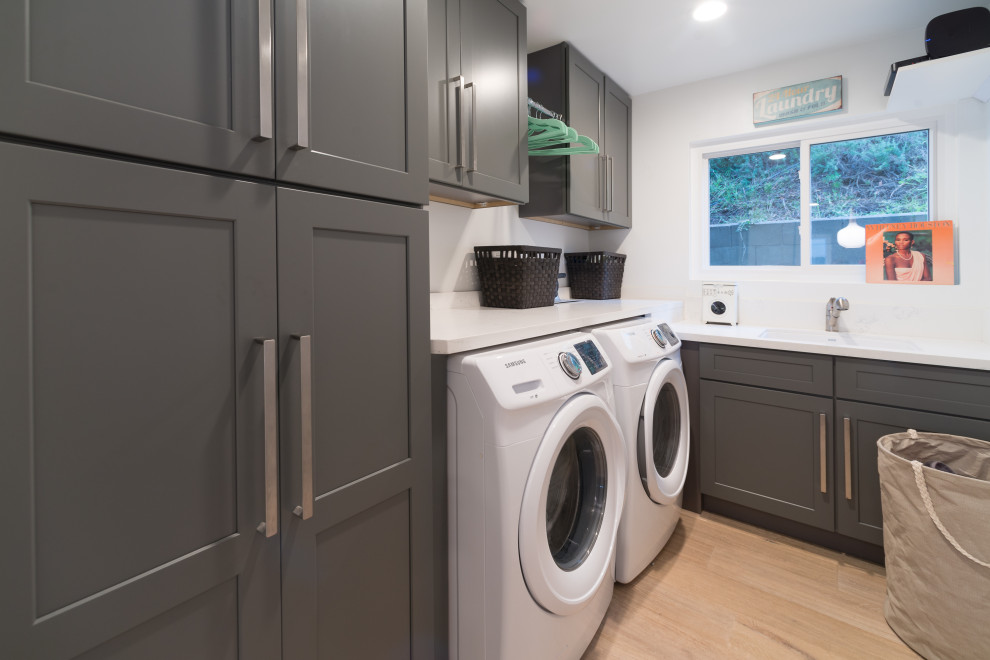 Design ideas for a mid-sized contemporary l-shaped utility room in San Diego with an undermount sink, shaker cabinets, grey cabinets, quartz benchtops, white walls, vinyl floors, a side-by-side washer and dryer, beige floor and white benchtop.
