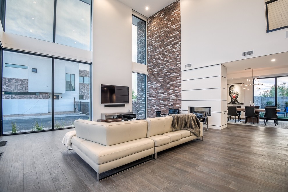 Large modern formal loft-style living room in Phoenix with multi-coloured walls, dark hardwood floors, a two-sided fireplace, a tile fireplace surround and a wall-mounted tv.