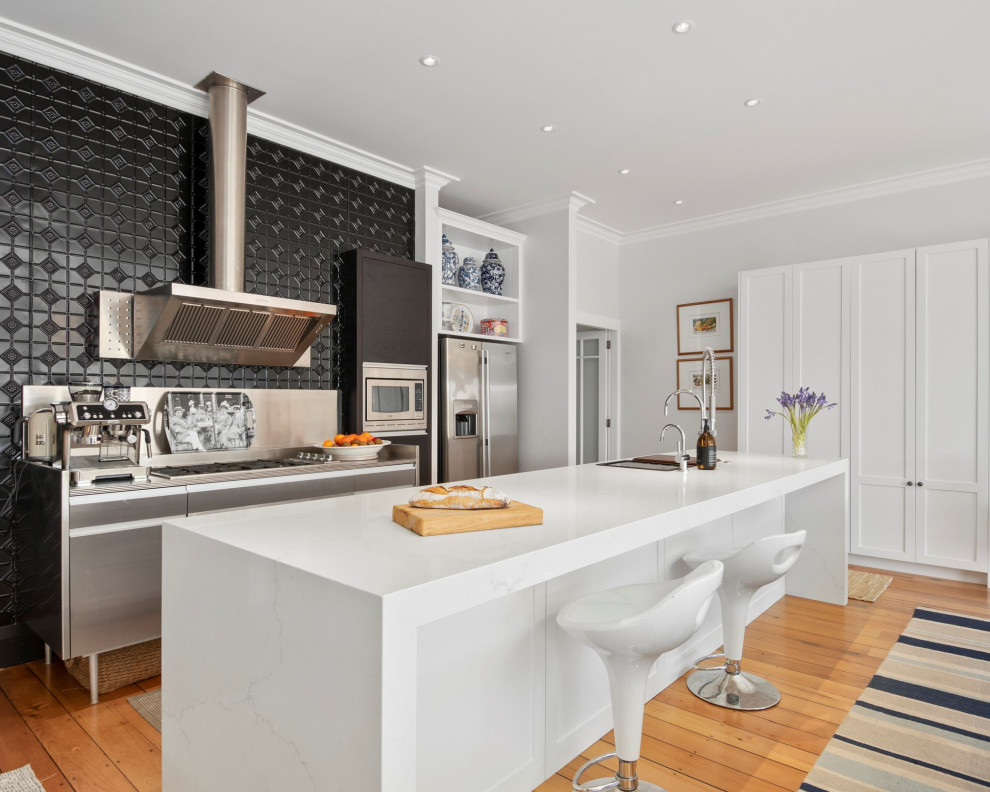 Inspiration for a medium sized victorian galley kitchen/diner in Auckland with composite countertops, black splashback, stainless steel appliances, medium hardwood flooring, an island, brown floors and white worktops.