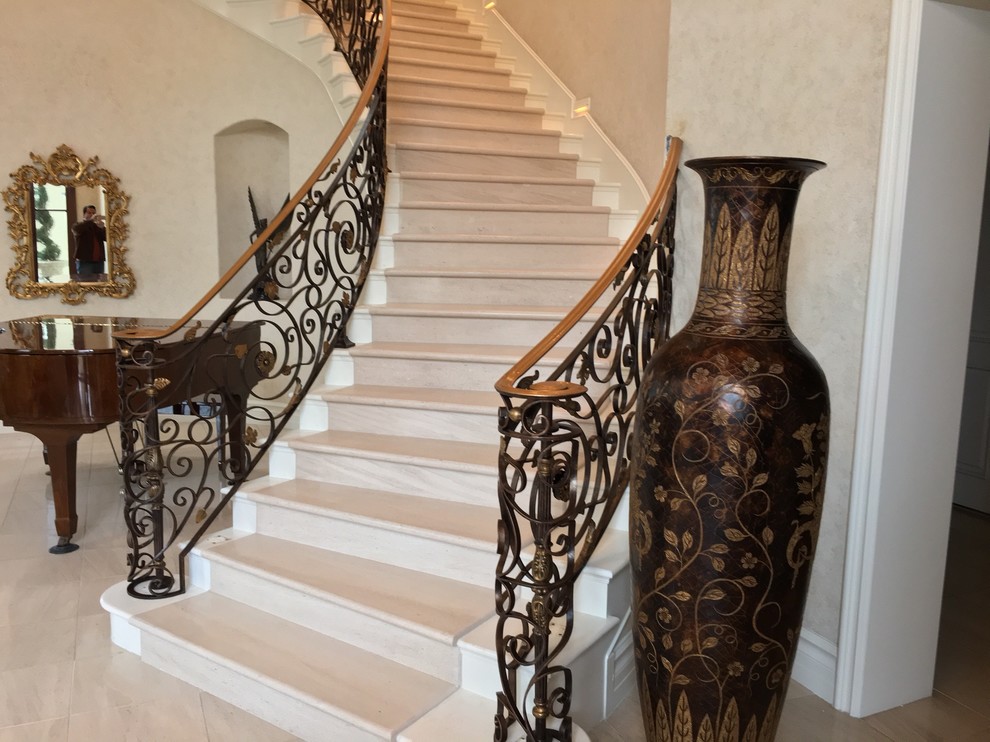 Large mediterranean limestone curved staircase in Orange County with limestone risers and mixed railing.