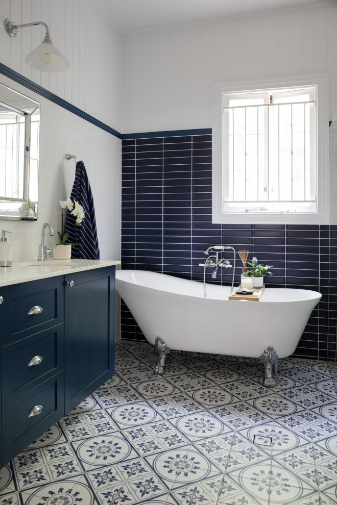 Photo of a mid-sized traditional master bathroom in Brisbane with shaker cabinets, blue cabinets, a claw-foot tub, blue tile, ceramic tile, white walls, ceramic floors, an undermount sink, engineered quartz benchtops, blue floor, white benchtops, a double vanity, a floating vanity and planked wall panelling.