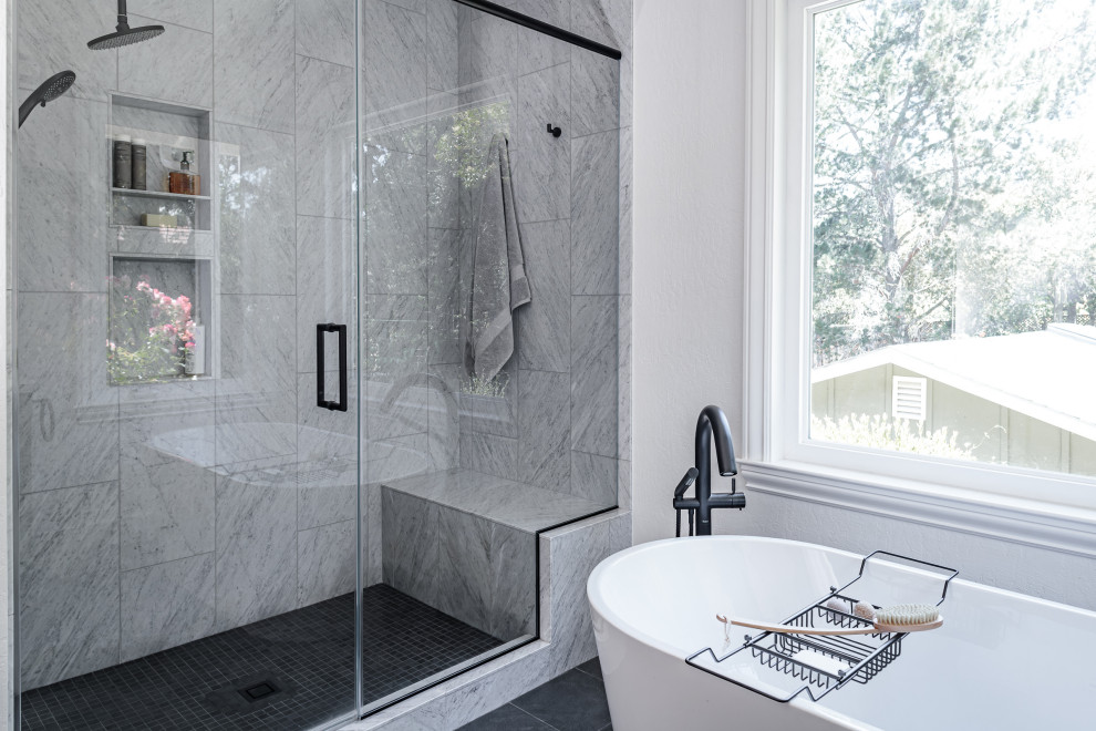 Cette image montre une salle de bain traditionnelle avec une baignoire indépendante, une douche double, des carreaux de porcelaine, un mur blanc, un sol en carrelage de porcelaine, un sol gris, une cabine de douche à porte battante et un banc de douche.