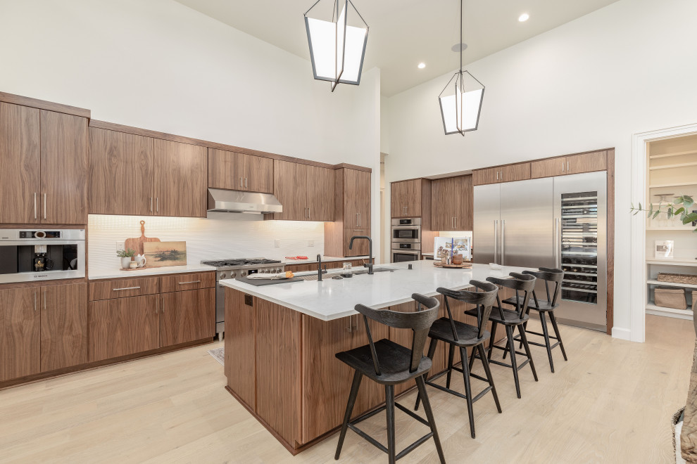Example of a mid-sized southwest l-shaped light wood floor and brown floor open concept kitchen design in Portland with an undermount sink, flat-panel cabinets, medium tone wood cabinets, quartzite countertops, white backsplash, ceramic backsplash, stainless steel appliances, an island and white countertops