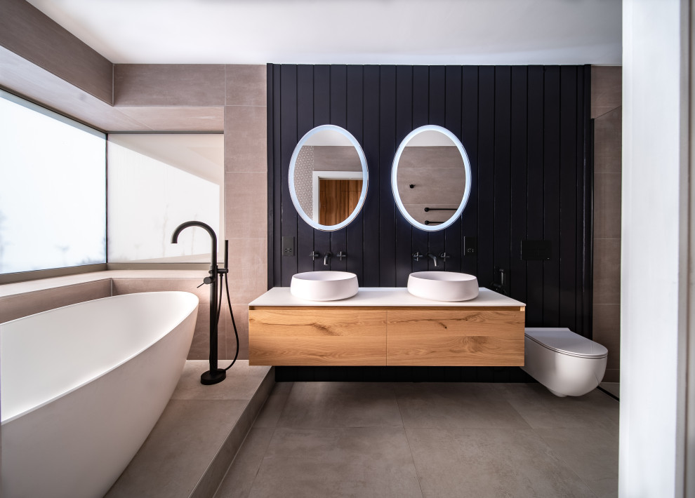 This is an example of a large modern bathroom in London with medium wood cabinets, a wall-mount toilet, brown tile, white benchtops, a double vanity and a floating vanity.