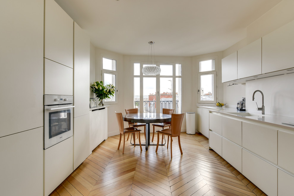 Design ideas for a large contemporary galley eat-in kitchen in Paris with an integrated sink, white splashback, panelled appliances, light hardwood floors, white benchtop, flat-panel cabinets, no island, beige floor and white cabinets.