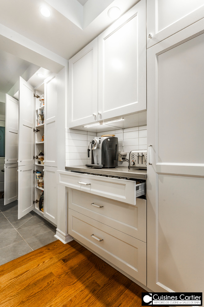 Eat-in kitchen - large transitional medium tone wood floor eat-in kitchen idea in Montreal with a double-bowl sink, shaker cabinets, white cabinets, quartzite countertops, white backsplash, ceramic backsplash, stainless steel appliances and an island