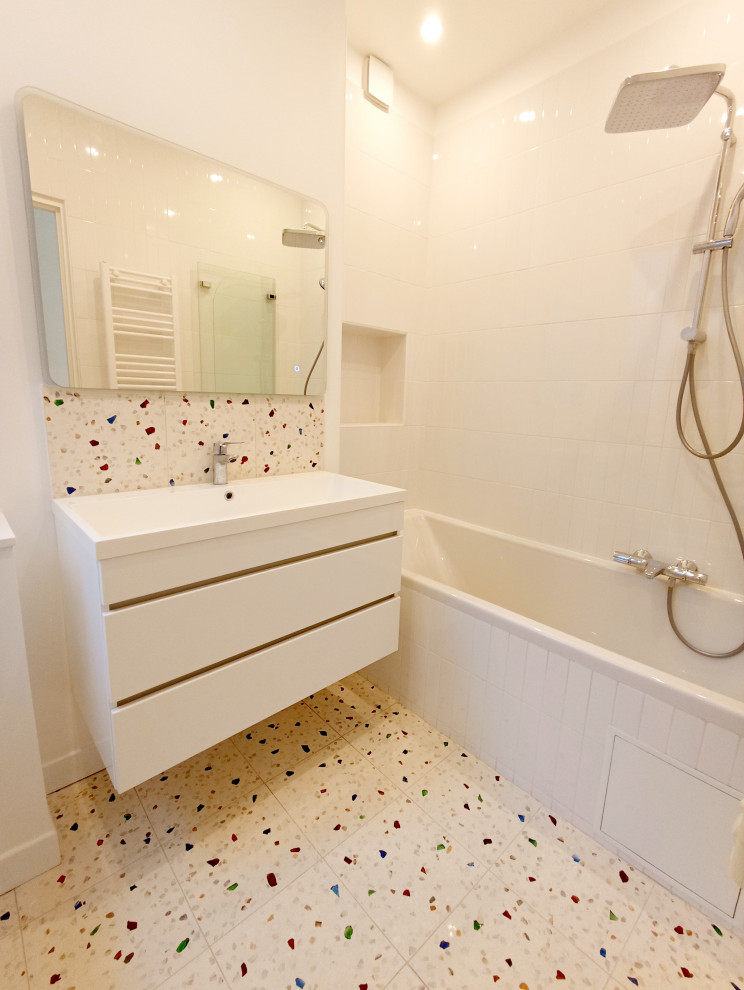 Стильный дизайн: детская ванная комната среднего размера в современном стиле с белыми фасадами, полновстраиваемой ванной, инсталляцией, белой плиткой, керамической плиткой, белыми стенами, полом из терраццо, раковиной с несколькими смесителями, белой столешницей, подвесной тумбой и тумбой под одну раковину - последний тренд