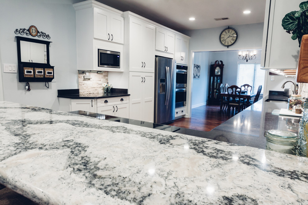 Inspiration for a large transitional galley light wood floor and brown floor open concept kitchen remodel with an undermount sink, shaker cabinets, white cabinets, quartz countertops, white backsplash, stone tile backsplash, stainless steel appliances and a peninsula