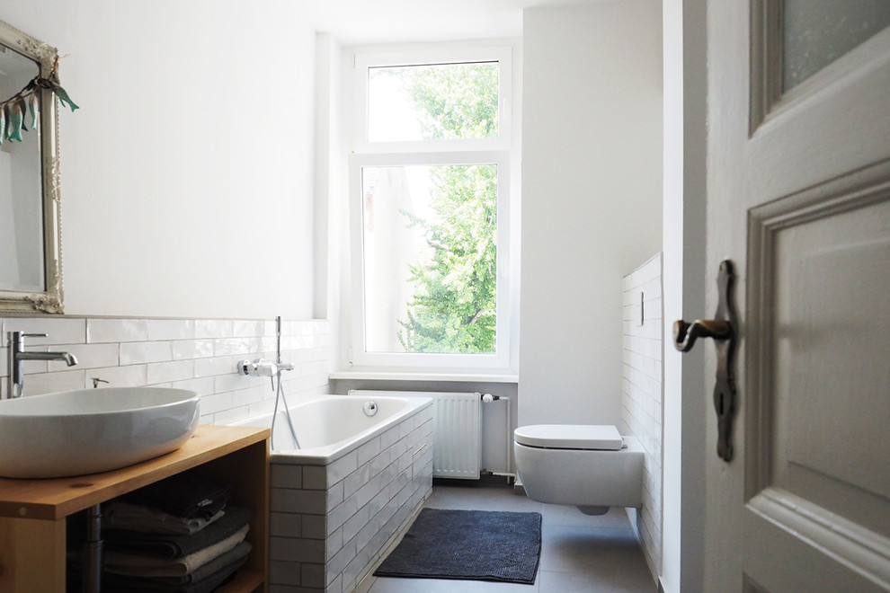 Inspiration for a small transitional bathroom in Berlin with a drop-in tub, a wall-mount toilet, a vessel sink and open cabinets.