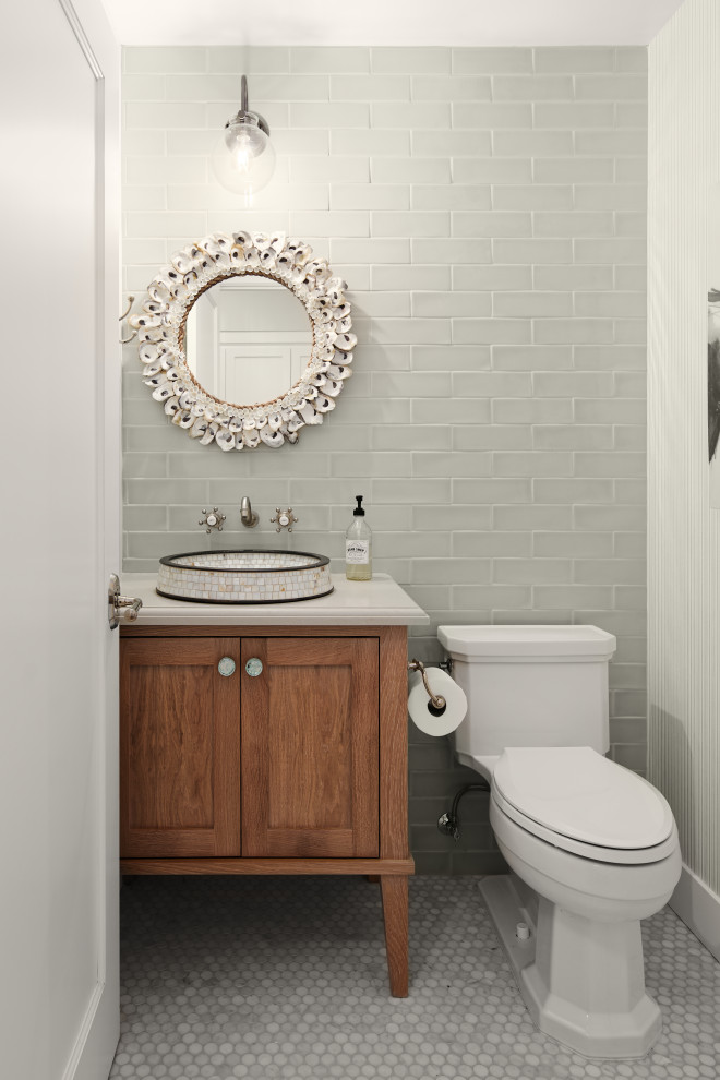 Photo of a mid-sized beach style powder room in San Francisco with furniture-like cabinets, medium wood cabinets, gray tile, subway tile, mosaic tile floors, a vessel sink, grey floor, beige benchtops, a two-piece toilet and grey walls.