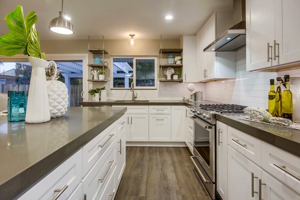 This is an example of a contemporary kitchen in Orange County with shaker cabinets, white cabinets, white splashback, subway tile splashback, stainless steel appliances, medium hardwood floors, with island, grey floor and grey benchtop.