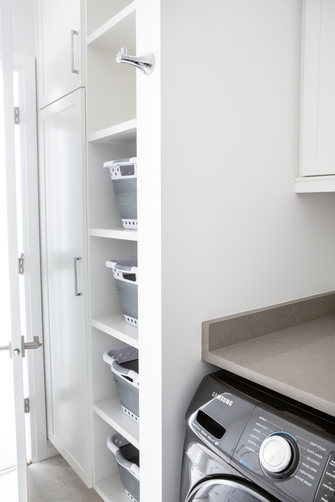 This is an example of a large transitional l-shaped dedicated laundry room in Vancouver with a single-bowl sink, shaker cabinets, white cabinets, quartz benchtops, grey walls, a side-by-side washer and dryer, grey floor and brown benchtop.