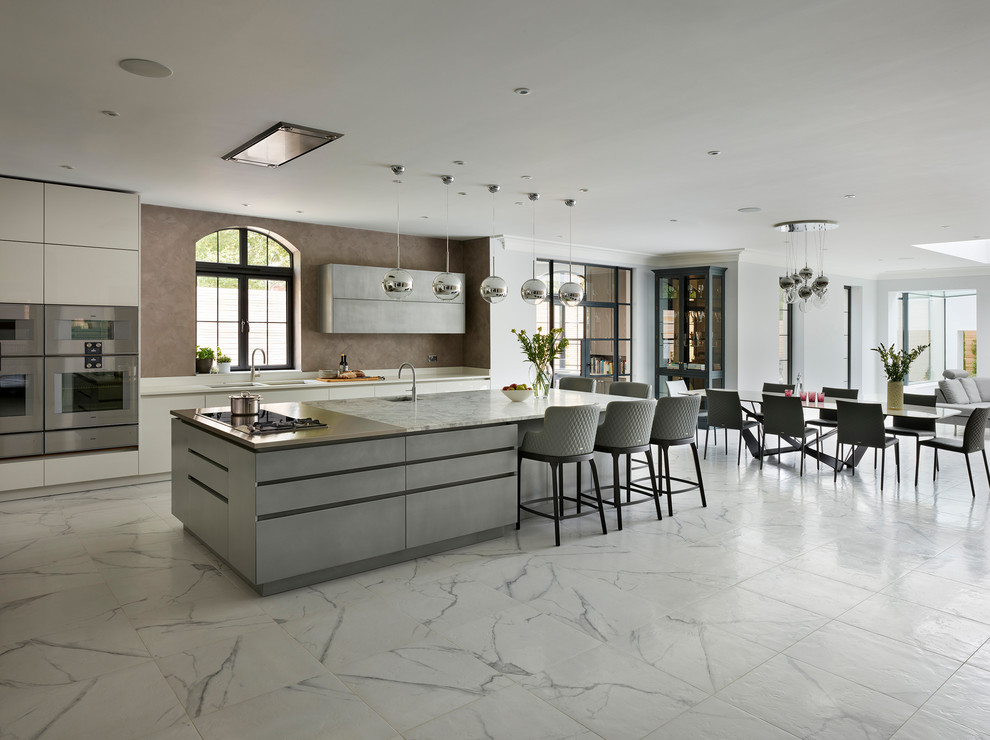 This is an example of an expansive contemporary open plan kitchen in London with flat-panel cabinets, white cabinets, granite benchtops, with island and white benchtop.