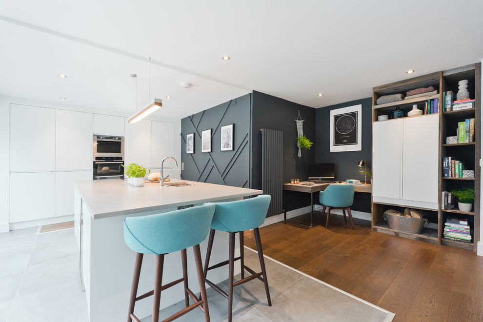 Contemporary l-shaped kitchen in London with an undermount sink, flat-panel cabinets, white cabinets, white splashback, panelled appliances, with island, grey floor and grey benchtop.
