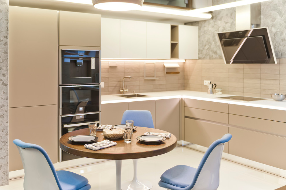 Contemporary l-shaped open plan kitchen in Moscow with an undermount sink, flat-panel cabinets, beige cabinets, glass benchtops, grey splashback, ceramic splashback, no island and black appliances.