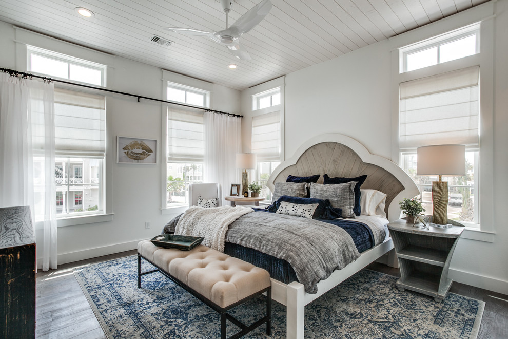 This is an example of a beach style bedroom in Austin with white walls, dark hardwood floors and brown floor.