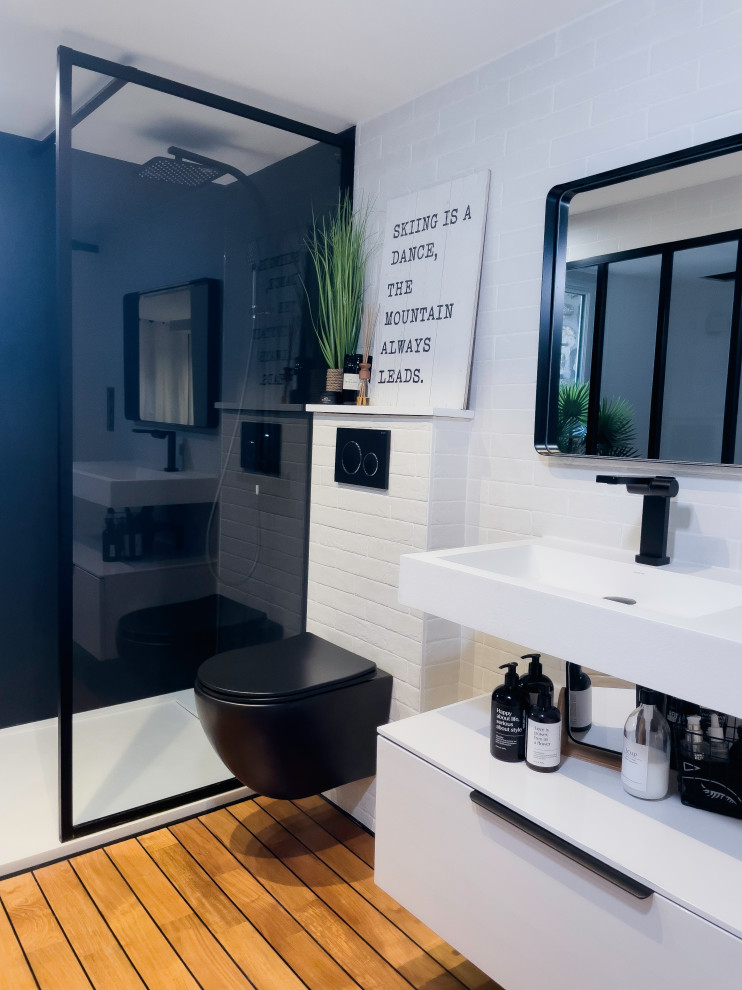 Modern inredning av ett mycket stort vit vitt badrum med dusch, med en kantlös dusch, en vägghängd toalettstol, vita skåp, vit kakel, tunnelbanekakel, vita väggar, ljust trägolv, ett konsol handfat och brunt golv
