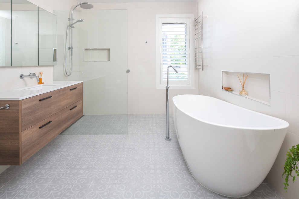 This is an example of a mid-sized contemporary bathroom in Brisbane with flat-panel cabinets, medium wood cabinets, a freestanding tub, an open shower, white tile, porcelain tile, white walls, porcelain floors, an undermount sink, engineered quartz benchtops, grey floor and white benchtops.