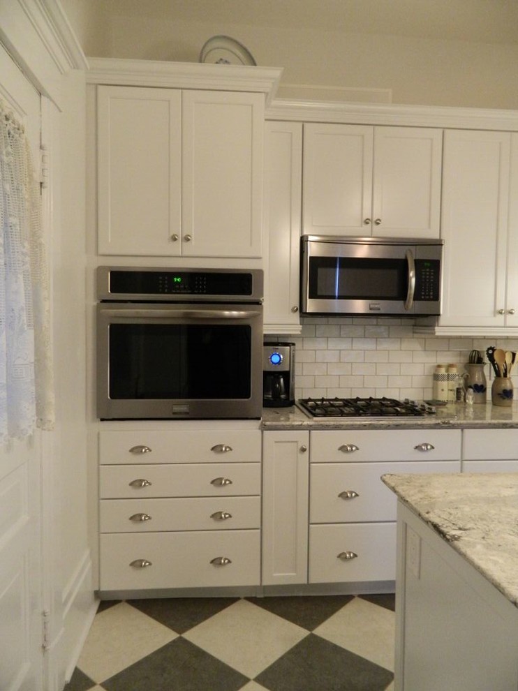 Example of a transitional enclosed kitchen design in Toronto with an undermount sink, recessed-panel cabinets, quartz countertops, white backsplash, ceramic backsplash, stainless steel appliances and an island