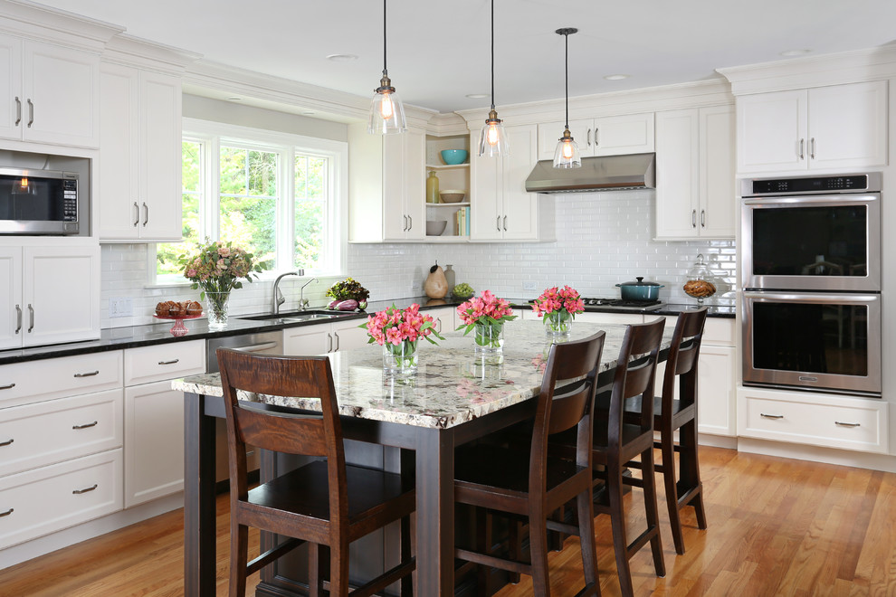 Inspiration for a mid-sized timeless l-shaped light wood floor eat-in kitchen remodel in Chicago with white cabinets, granite countertops, white backsplash, subway tile backsplash, an island, an undermount sink and stainless steel appliances