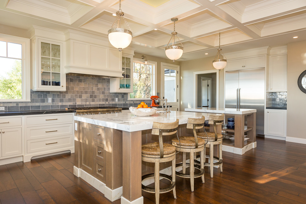 Inspiration for a huge transitional l-shaped medium tone wood floor and brown floor eat-in kitchen remodel in Orange County with a farmhouse sink, white cabinets, marble countertops, blue backsplash, ceramic backsplash, stainless steel appliances, two islands and shaker cabinets