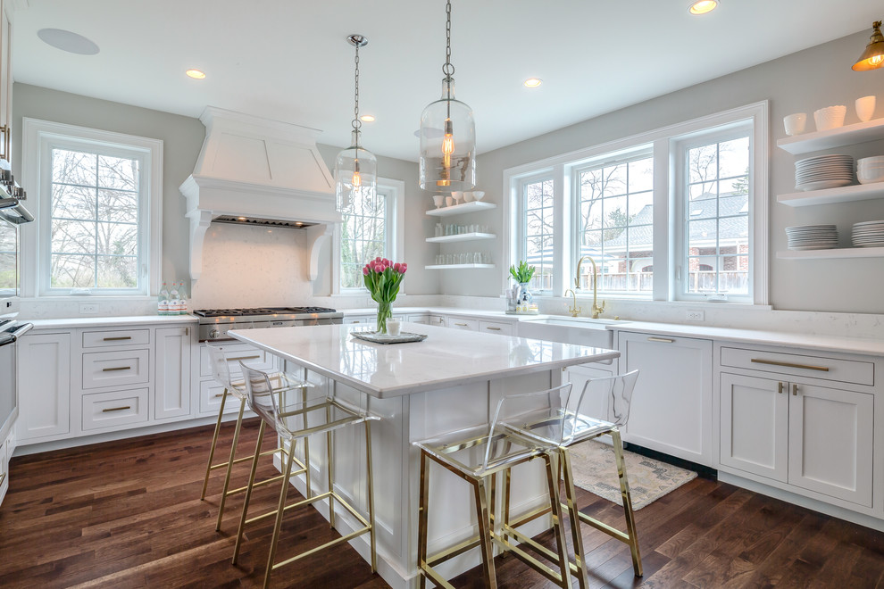 This is an example of a transitional u-shaped kitchen in Philadelphia with a farmhouse sink, shaker cabinets, white cabinets, panelled appliances, dark hardwood floors, with island, brown floor and white benchtop.