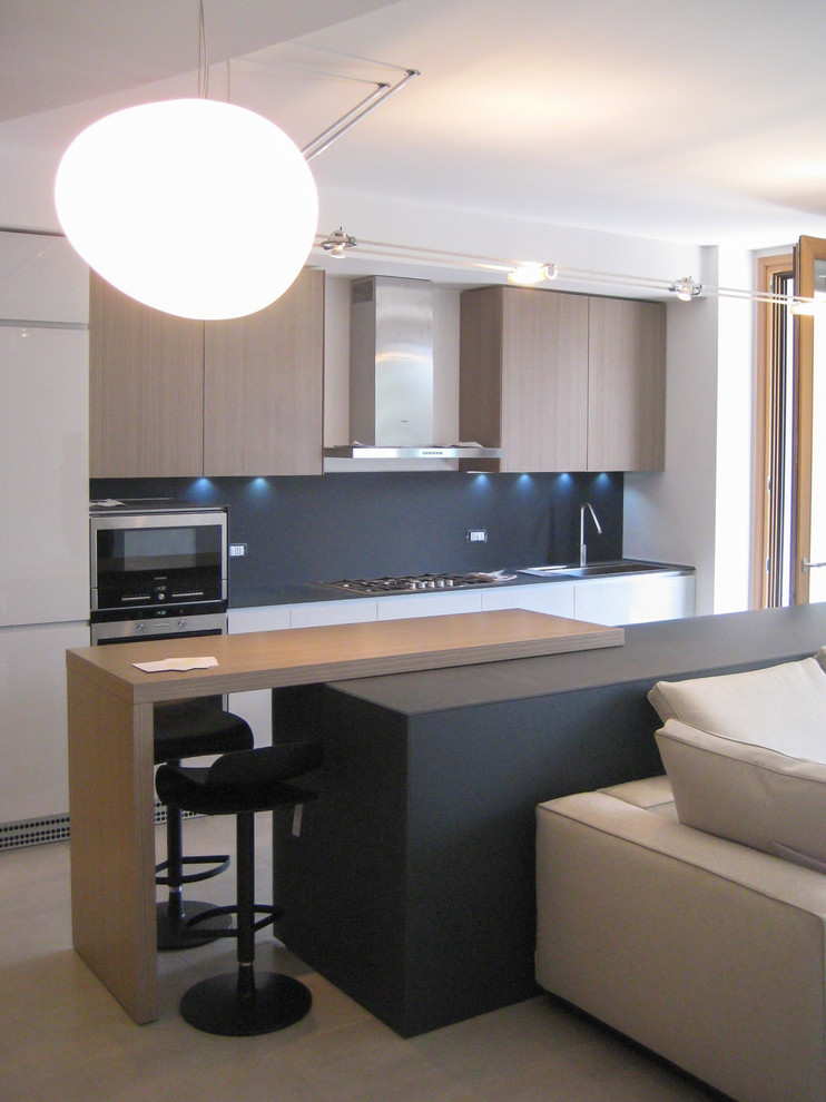 Small modern galley eat-in kitchen in Milan with porcelain floors, beige floor, a drop-in sink, flat-panel cabinets, glass benchtops, grey splashback, glass sheet splashback, stainless steel appliances, with island and grey benchtop.