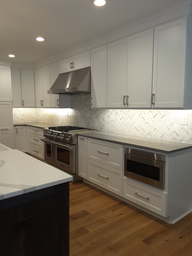 Large modern l-shaped open plan kitchen in Philadelphia with shaker cabinets, white cabinets, quartz benchtops, white splashback, with island and grey benchtop.