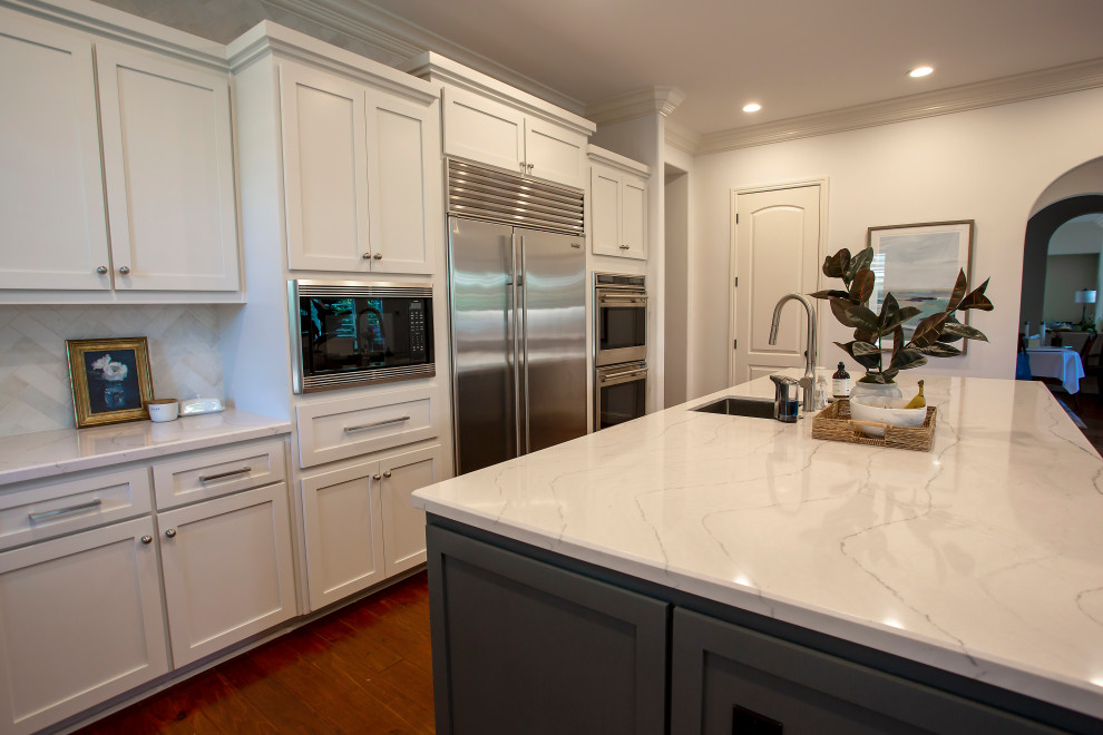 Idéer för ett stort modernt vit kök, med en undermonterad diskho, skåp i shakerstil, vita skåp, bänkskiva i kvarts, vitt stänkskydd, stänkskydd i porslinskakel, rostfria vitvaror, mellanmörkt trägolv, flera köksöar och brunt golv