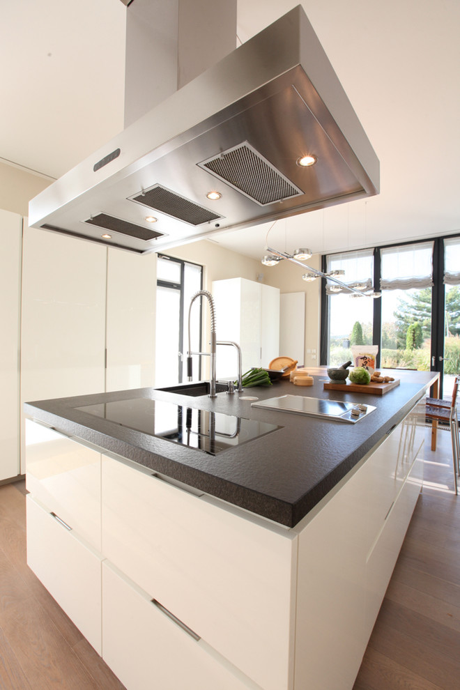 Inspiration for a large contemporary eat-in kitchen in Frankfurt with white cabinets, granite benchtops, flat-panel cabinets, medium hardwood floors, an undermount sink, panelled appliances and with island.
