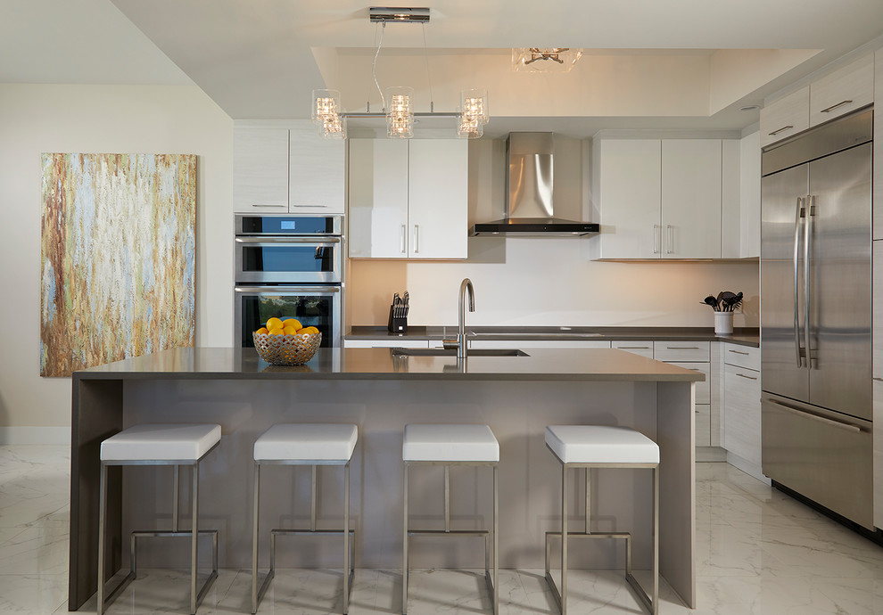 Design ideas for a contemporary l-shaped kitchen in Miami with a single-bowl sink, flat-panel cabinets, white cabinets, white splashback, stainless steel appliances, with island and white floor.