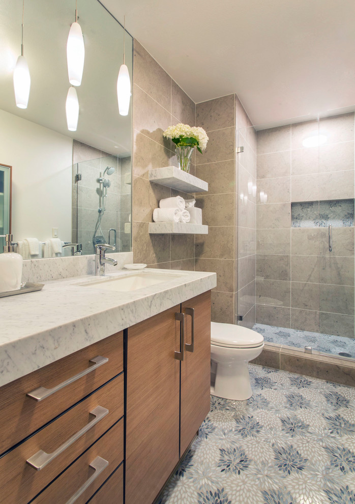 This is an example of a mid-sized contemporary master bathroom in San Diego with medium wood cabinets, an alcove shower, beige tile, stone tile, grey walls, mosaic tile floors, an undermount sink, marble benchtops, multi-coloured floor, a hinged shower door, flat-panel cabinets and a one-piece toilet.