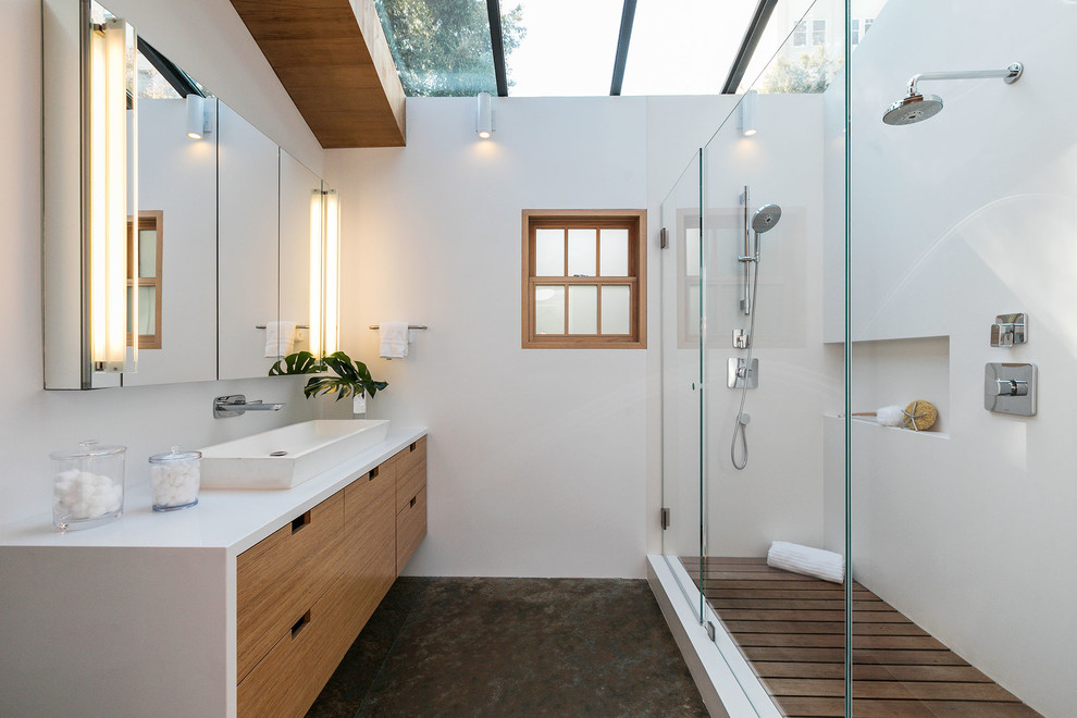 This is an example of an eclectic master bathroom in San Francisco with flat-panel cabinets, medium wood cabinets, a corner shower, a one-piece toilet, white tile, stone slab, white walls, slate floors, a vessel sink, engineered quartz benchtops, multi-coloured floor, a hinged shower door and white benchtops.