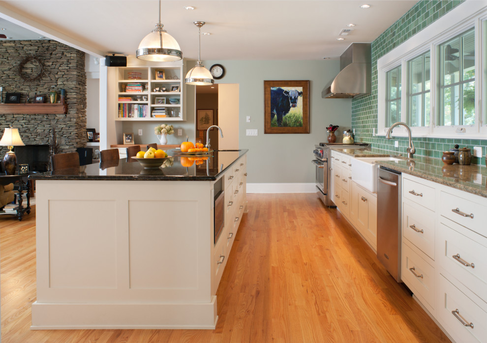 Open concept kitchen - large transitional medium tone wood floor and brown floor open concept kitchen idea with a farmhouse sink, shaker cabinets, white cabinets, green backsplash, subway tile backsplash, stainless steel appliances and an island